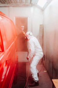 automotive industry manufacturing - mechanic engineer using spray gun and painting a red car