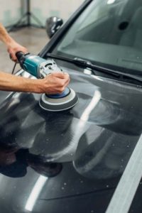 Male person with polishing machine cleans car. Auto detailing on carwash station, restore the paint of vehicle