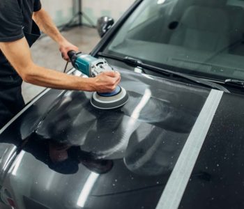 Male person with polishing machine cleans car. Auto detailing on carwash station, restore the paint of vehicle