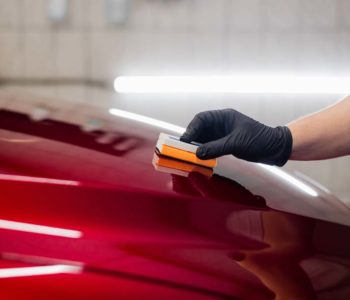 Man worker of car detailing studio applying ceramic coating on car paint with sponge applicator